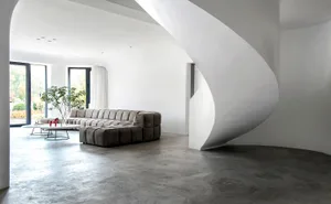 A minimalist living room featuring modern furniture, a concrete floor, and large windows.