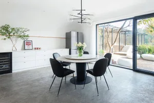 A modern dining room with a concrete floor and white walls, featuring a round table with a black base and black chairs, and a