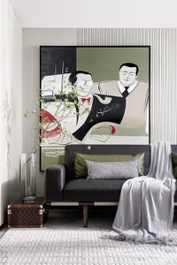 A modern living room featuring a large abstract painting of two men, a sleek gray sofa adorned with olive green and gray cush