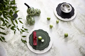 Modern green ceramic dinnerware with red napkins and green apples on a light, textured table surface.