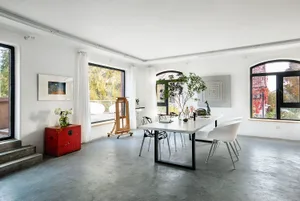 A spacious, modern dining room featuring a white table, white chairs, and a concrete floor with arched windows, artwork, and