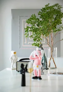 A modern interior space with decorative plastic figures, a green plant, and a silver speaker on a white surface