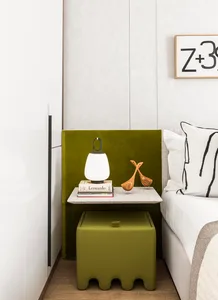 A minimalist bedroom featuring a green nightstand with a lamp, books, and wooden figurines.