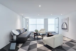Modern minimalist living room with a geometric patterned floor, white walls, and white and black furniture, featuring a large