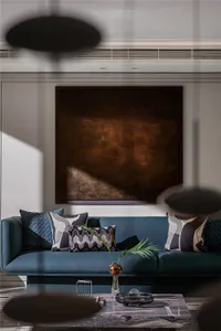 A modern living room featuring a blue leather sofa adorned with decorative pillows, placed against a wall with a large abstra