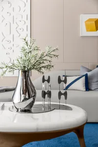 Modern living room with metallic candlesticks and greenery on a white and brown table against a beige sofa and wall.