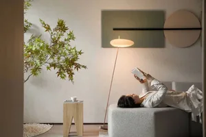 A modern living space with neutral-toned furniture and decor, including a reading person lying on a cushion under a floor lam