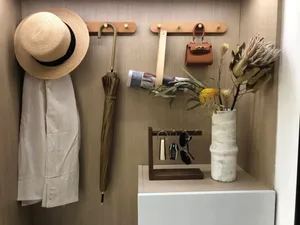An entry-way adorned with a dried-flower arrangement in a white vase, a wooden coat rack, and a beige hat hanging.
