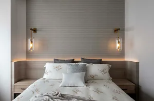 A minimalist bedroom with a bed adorned with floral-patterned bedding, grey pillows, and bedside lamps.