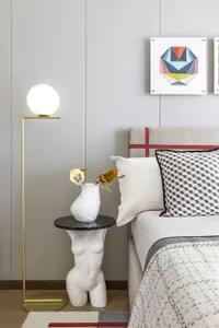 A modern minimalist bedroom with a white and red bed, a white vase with flowers on a black marble table, a spherical floor la