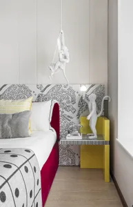 A modern bedroom featuring a monkey-shaped lamp hanging above the bed, with a patterned bedspread and a small bedside table.