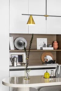 Modern kitchen with sleek white cabinets, metallic lighting fixture, and decorative vase on white table.