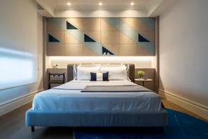 Minimalist bedroom with gray upholstered bed, geometric wall paneling, and blue rug on hardwood floor.