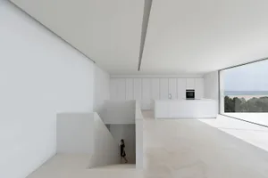 A minimalist white kitchen with modern design elements, large windows, and an open floor plan.