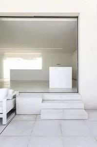 A minimalist living room with concrete flooring and stairs leading up to a modern interior.