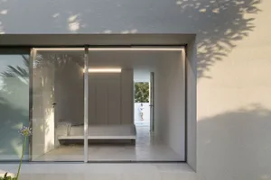 A minimalist bedroom with a concrete floor and walls, featuring a bed and minimal furniture.