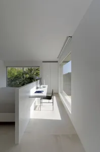 A minimalist office space in white with a desk, chair, and window.