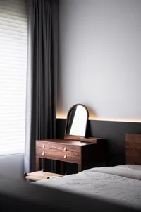 A minimalist bedroom featuring a wooden console table with a built-in mirror and drawers, complemented by natural light strea