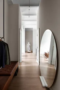 A modern corridor featuring a wooden floor, a large oval mirror, and a statue.