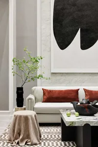 Modern living room with marble coffee table, white sofa with orange cushions, and abstract black and white painting on the wa