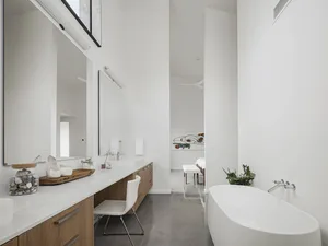 Modern minimalist bathroom with white walls, a white bathtub, and a sleek wooden vanity.