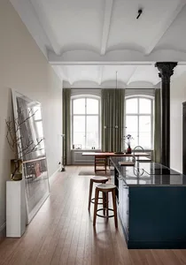 A modern kitchen with dark wood flooring, green curtains, and a dark blue kitchen island.