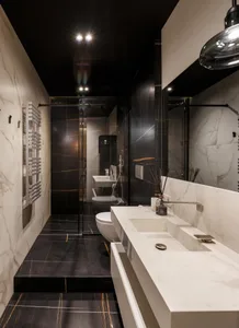 A modern bathroom featuring white marble walls, black marble floor, and a white countertop sink with a black faucet.