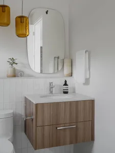A modern minimalist bathroom with a wooden cabinet, white marble sink, and a framed mirror.