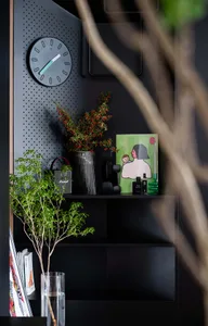 A modern black metal pegboard shelf unit adorned with various decorative items, including a clock, plants, and books.