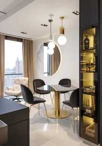 Modern, sleek, white kitchen and dining area featuring black marble table and gold-brass chairs, illuminated by pendant light