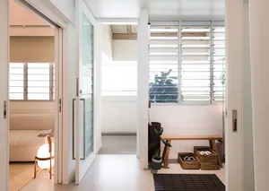 A modern, minimalist living room with light-colored walls and furniture, featuring natural light from large windows and a cle