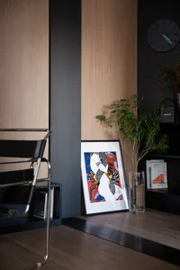 A framed abstract artwork featuring bold colors and shapes, placed next to a potted plant in a corner of a room with wooden p