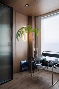 Modern living room featuring wood elements, a contemporary chair, and a wall-mounted light fixture with a plant.