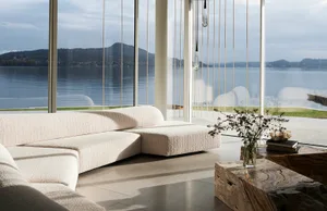 Modern minimalist living room with a white textured fabric couch, large windows overlooking a serene lake view.