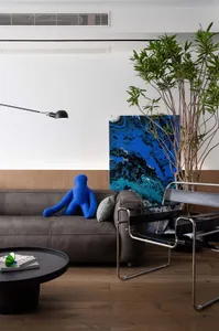 Modern living room with a leather sofa, a blue figure, a black and blue painting, and a potted plant.