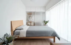 Modern minimalist bedroom with wooden bed frame and glass closet doors.