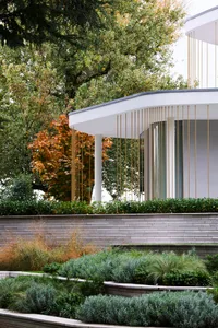 A modern residential exterior featuring a white stone facade and greenery.