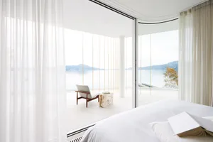 A modern white bedroom featuring minimalist decor and a view of the lake through large windows.