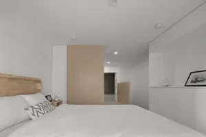 A minimalist bedroom with white walls, a wooden bed frame, and a modern design.