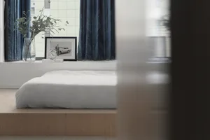 Minimalist bedroom with a wood frame bed, white bedding, and blue curtains.