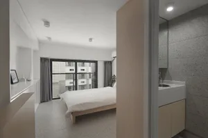 A minimalist bedroom with concrete walls and glass doors, featuring a bed with white bedding and a wooden headboard.