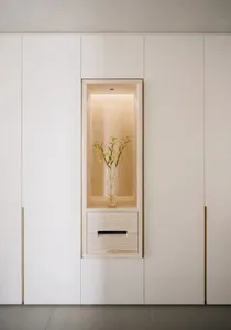 A minimalist interior wall niche with a wooden frame, illuminated light, and a vase of flowers.