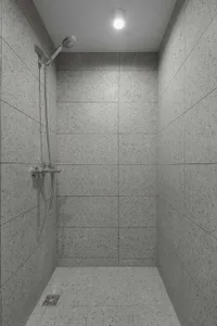 A minimalist shower area with concrete tiles walls and floor, featuring a shower head mounted on the wall and a ceiling light