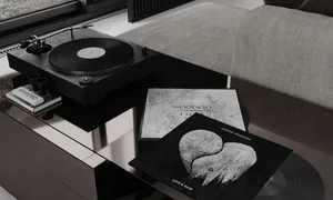 A modern living room with glass windows, a stylish coffee table with vinyl records and album covers, and a comfortable sofa.