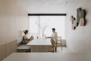 A modern living room featuring minimalist design with wooden furniture, fabric seating, and plaster walls.