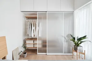 A minimalist bedroom with a glass sliding door, white furniture, and light wood flooring.