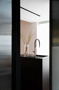A modern minimalist kitchen with a transparent window featuring a vase with branches, a sleek faucet, and a minimalist aesthe