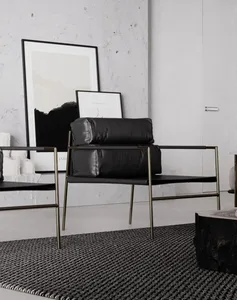 A modern minimalist living room with black leather and gold metal furniture, concrete flooring, and framed pictures on a text