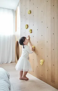 A young child plays on a wooden climbing wall in a modern playroom.