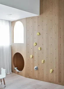A modern children's playroom featuring a wooden climbing wall with colorful grips and a circular cutout for a cozy nook.